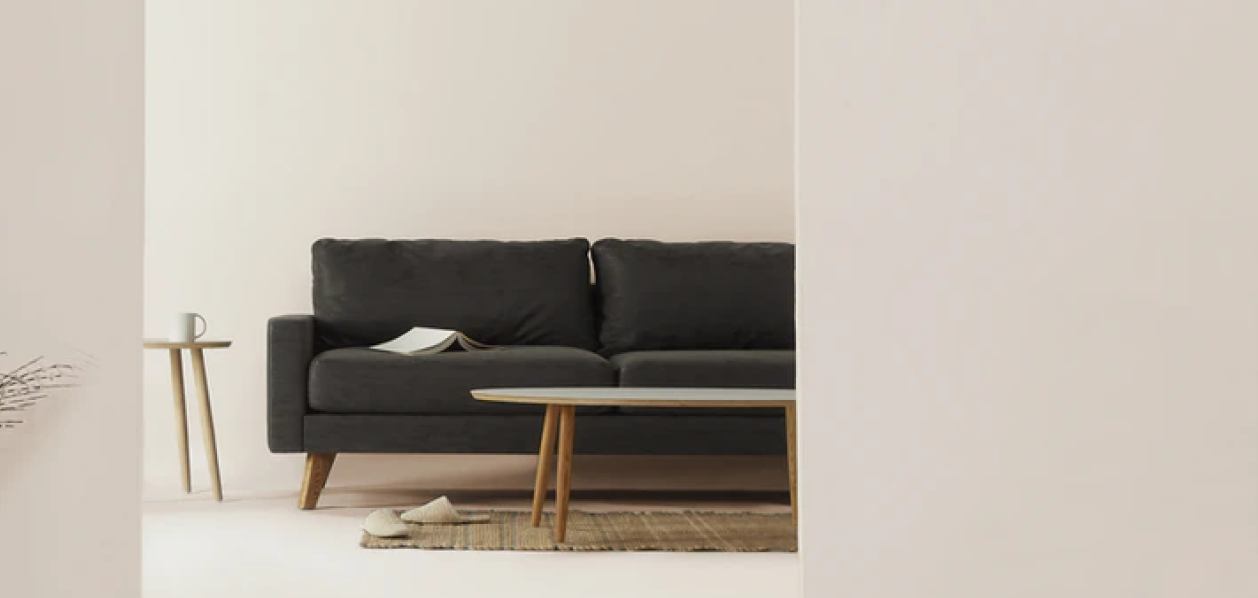 Sala con un sofá negro y un cuaderno encima de él, alfombra, pantuflas, dos mesas y una taza