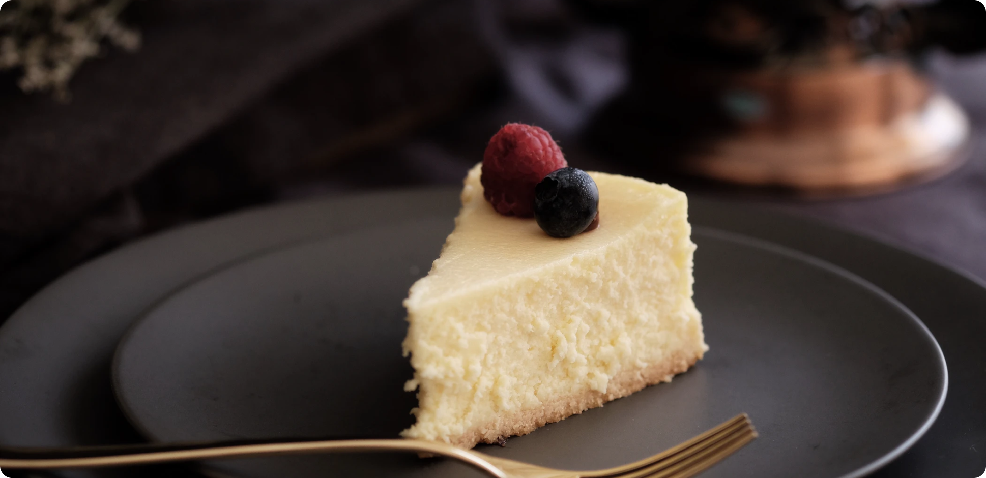 A slice of cheesecake on top on a black plate with blurred background | Una rebanada de tarta de queso encima en un plato negro con fondo difuminado